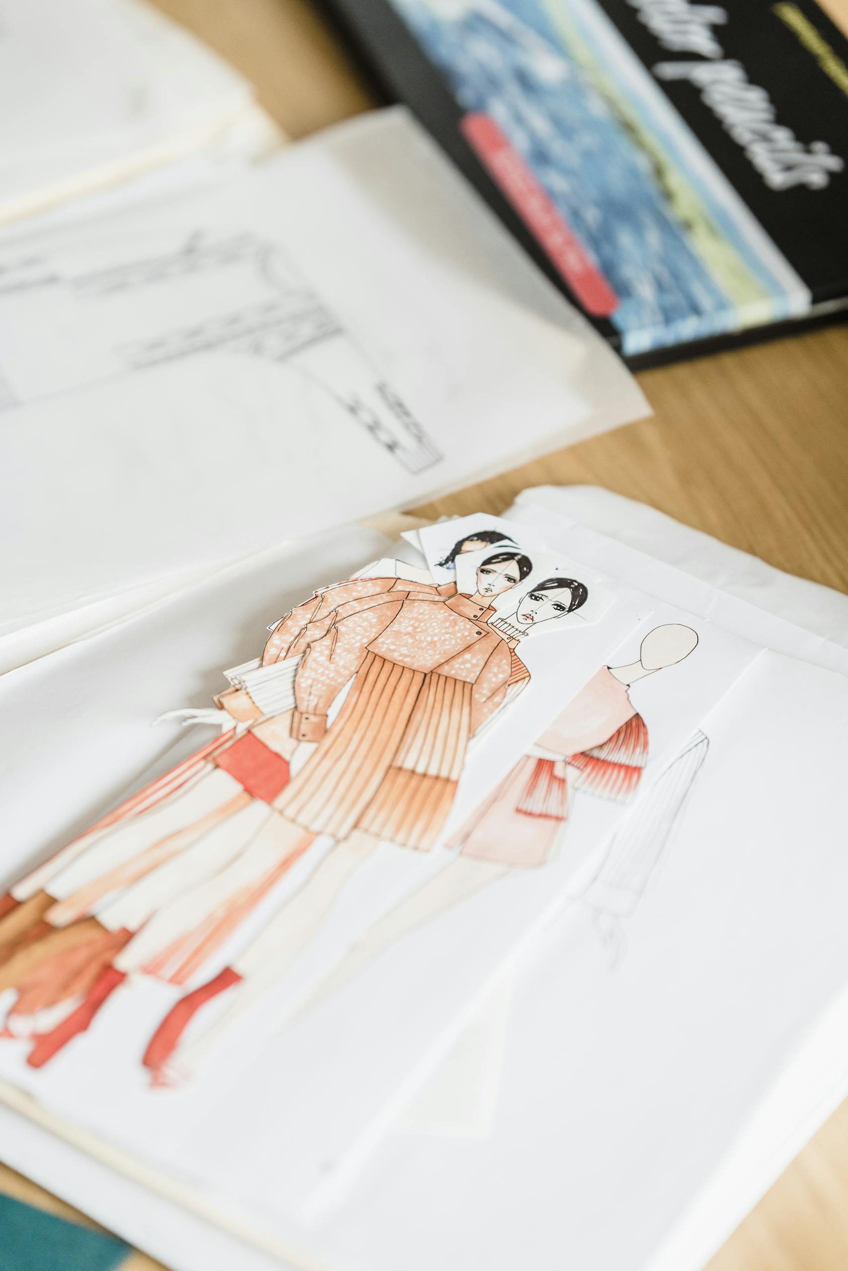 Colorful creative drafts of stylish garments placed on white paper on wooden table with patterns and drafts in modern workshop